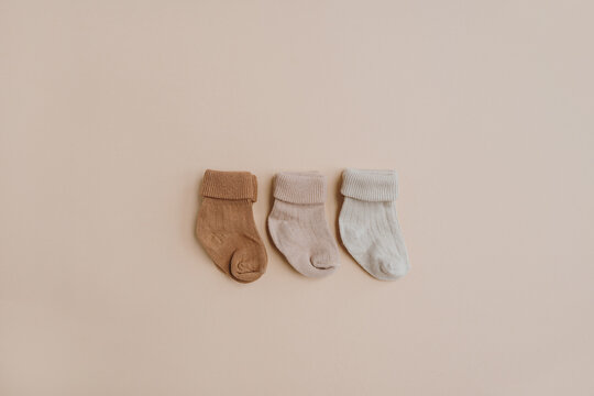 Cozy hygge pastel colourful newborn baby socks on neutral beige background. Aesthetic minimalist baby fashion collage. Happy maternity concept