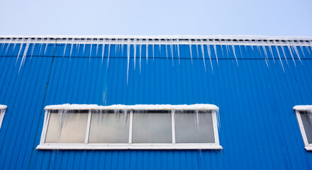 The metal roof of the production room is covered with icicles. Danger of snow and ice coming down on your head. Icicles overhead.