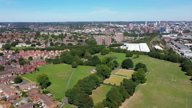 Aerial drone footage of a British park in the village of Wortley in Leeds showing the park and residential houses with blocks of flats, filmed on a sunny summers day in the summer time.