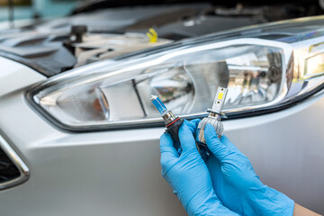 Close-up photo of a man's hands holding a car light bulb near the car for replacement. © RomanR