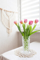 Beautiful pink tulips in glass vase against handmade macrame wallhanging.  ECO friendly modern concept in the interior.