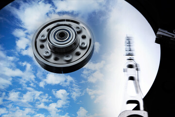 Cloud storage or cloud drive concept image. Hard disk (HDD or Hard drive) with clouds and sky reflecting on disk. Head and Axis with motion blur.