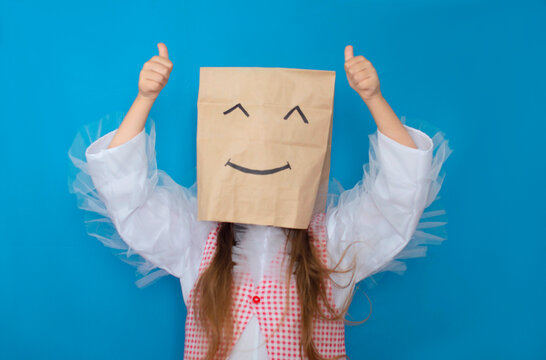 girl hides her face behind a happy emoji smile. Photo of an anonymous lady incognito holding a smiley face wearing a plaid shirt against an isolated blue background. He points his finger up