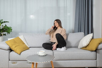 Happy young woman caller talking on the phone at home, cheerful teen girl enjoys pleasant mobile conversation, smiling millennial female holding cell speaking making call by telephone in living room