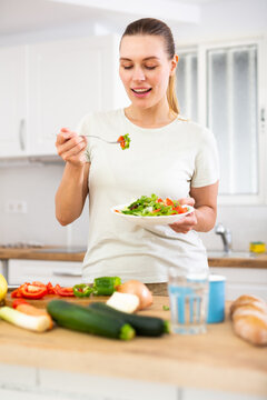 Portrait of woman standing in home kitchen and tasting vegetable salad
