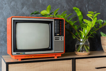 Old orange TV on a wooden cabinet in the room of the house. Loft wall. Warm atmosphere.