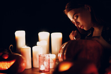 Young woman making Halloween pumpkin Jack-o-lantern with candles in dark. Female hands cutting pumpkins with knife