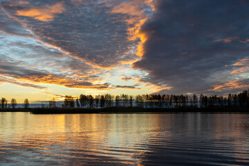 Fototapeta na wymiar Beautiful lake at sunrise, golden hour sunrise, sunlight and grand cloud reflections on water, colorful dramatic sky at sunrise, dark silhouettes of trees, motion blur