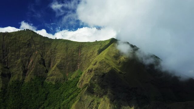 View from above, stunning aerial view of a green mountain range surrounded by clouds and a beautiful blue sky in the background. Sembalun, Lombok, West Nusa Tenggara, Indonesia. 