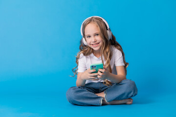 Fototapeta na wymiar girl in jeans, white T-shirt is sitting with a smartphone in her hands on a blue background