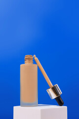 Opened Bottle with foundation liquid beige cream on stand, white podium. Professional makeup product for perfect complexion. Woman accessories, base beauty product, primer, concealer..