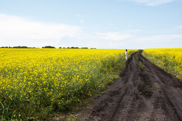 woman stands on a dirt road in a rapeseed field
