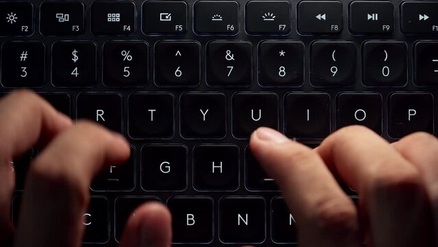 Close up and top view footage of young businessman hands busy working, searching and studying by typing on glowing keyboard in the dark for send emails and surf on a web browser,