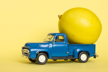  Car toy blue pickup and lemon on a yellow background, delivery of vegetables and fruits, vitamins in autumn, winter and spring, selective focus