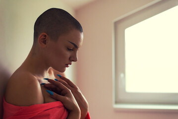 Young depressed female cancer patient standing in hospital beside window