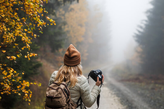 Woman with camera hiking in misty autumn forest. Photographing nature