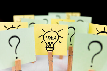 Light bulb doodle drawn on sticky note among many question marks. Hand drawn doodle lineart. Ideas,...