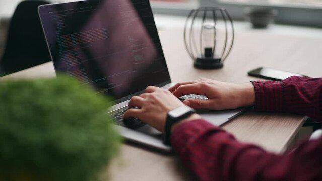 Close up of freelancer's hands typing code on laptop keyboard. Camera slides around developer's figers writing program code on computer display in slow motion. Programmer working on application.