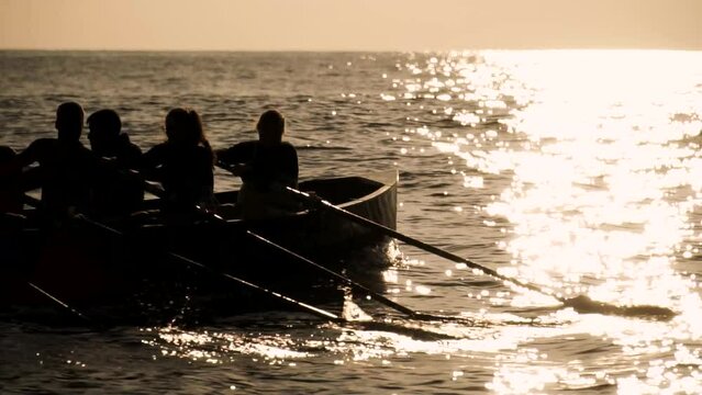 Silhouette of motivated people rowing together on a boat at sunset or sunrise