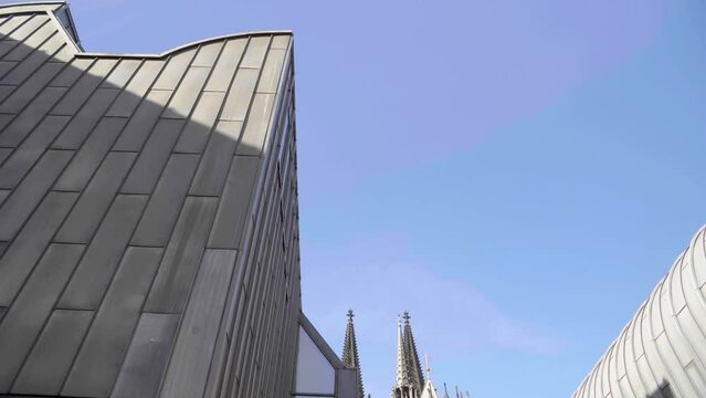 Backward dolly shot, tilting down from a modern steel sided building to reveal a medieval cathedral with flying buttresses and ornate spires 