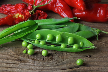 GREEN PEAS IN A POD WITH RED RIPE CHILIS AND A FEW LOOSE PEAS ON A WOODEN BOARD