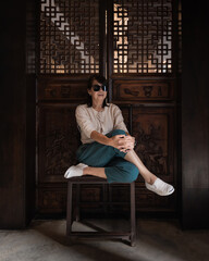 Beautiful portrait of an Asian senior woman sitting on an old wooden chair in a casual clothing fashion dress in a retro classic house background vintage style.