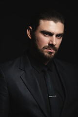 Portrait of a white Caucasian male brunet in a black classic suit, black shirt and black tie over a...