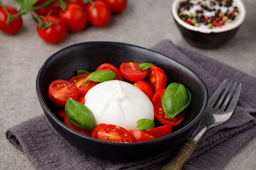Burrata cheese with tomatoes and basil on a gray kitchen table.