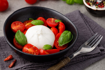 Burrata cheese with red tomatoes and green basil in a plate on a gray stone kitchen table, top view. Cheese ball burrata from mozzarella and cream. Italian food