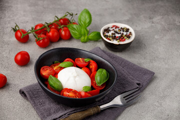 Burrata cheese with tomatoes and basil on a gray kitchen table, close up.