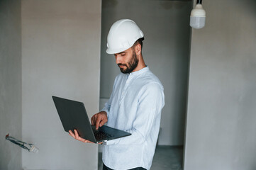 Holding laptop in hands. The man is making repairs in the apartment