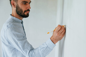 Doing marks by pencil on the wall. The man is making repairs in the apartment