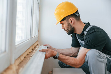 Installing a window sill. The man is making repairs in the apartment