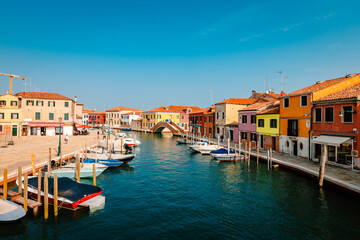 Fototapeta na wymiar Murano canal with colorful houses, moored boats and tourist walking
