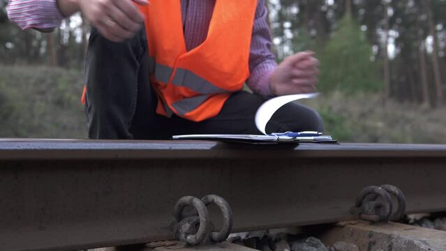 The railway transport inspector takes measurements with a tape measure of the railway track and makes entries in the log.