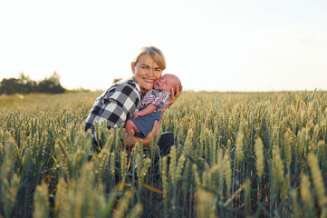 In the wheat. Happy woman on the agricultural field is with little baby in the hands