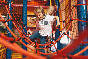 Excited kids playing together on net ropes. Happy group of siblings playing together on indoor...