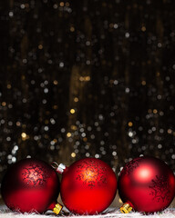 Christmas decorations composition view of three red evening balls with red glitter snowflakes on it on dark background with silver and gold colors bokeh. Holiday concept with copy space on top