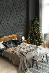 Cozy bedroom decorated for Christmas. A double bed with festive pillows and blankets against the backdrop of a large green Christmas tree, decorated with garlands and golden toys. Christmas morning