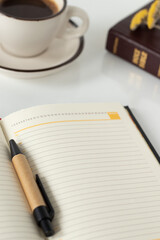 Notebook, pen, Holy Bible Book, and coffee cup on white background with copy space. Vertical shot, a close-up. Christian writing, planning, studying concept.