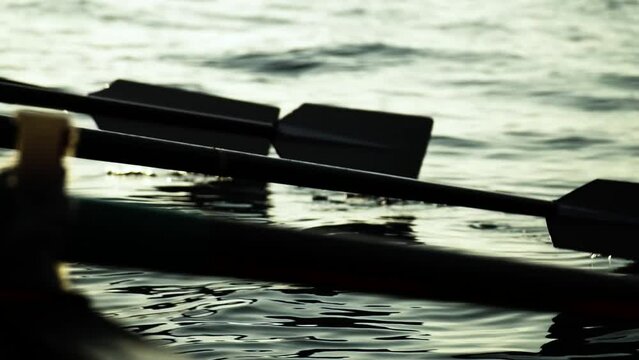 Close up on silhouette of rowing paddles in oarlocks propelling boat over water