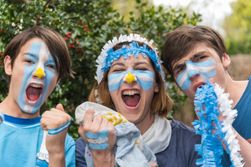 Familia con la cara pintada con los colores de la bandera Argentina, felices alentando al seleccionado en los partidos del mundial de futbol.  - obrazy, fototapety, plakaty
