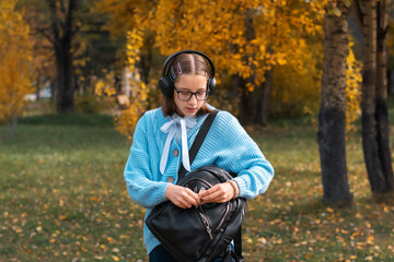 A young schoolgirl with a backpack and headphones is walking down the street listening to music.