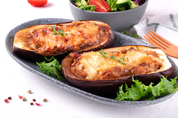 Stuffed eggplant halves with roasted vegetables, champignons and cheese served on the gray plate. Hot vegetarian meal