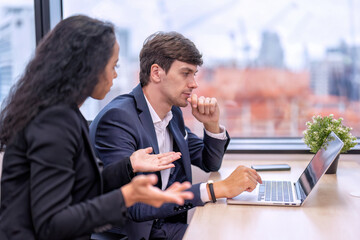 Staff employee sitting in work place close to window near construction site and overhead crane work in background look at computer screen and discussion on the work