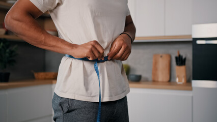 Unrecognizable sporty male sports man African guy measures waist with measuring tape check weight...