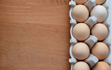 Chicken eggs in a cardboard box on a wooden table. Copy space.