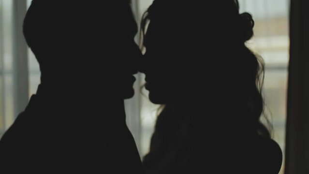 Silhouette of a man and woman in love kissing by the window, tenderness. Medium shot Silhouette of newlywed couple. Marriage, romantic atmosphere.