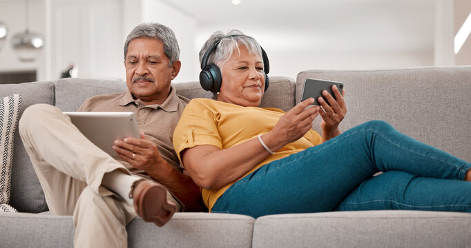 Senior couple, relax with technology and tablet, smartphone and headphones, streaming and watching online with 5g network. Elderly, man and woman with device, sofa and together in retirement. - Powered by Adobe