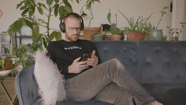 Medium close front angle of a man sitting on a couch scrolling and swiping and typing on an Iphone.